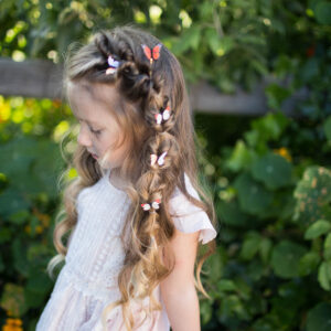 Side view of a young girl with hair standing outside modeling "Flip Faux Fishtail" hairstyle with butterfly accessories