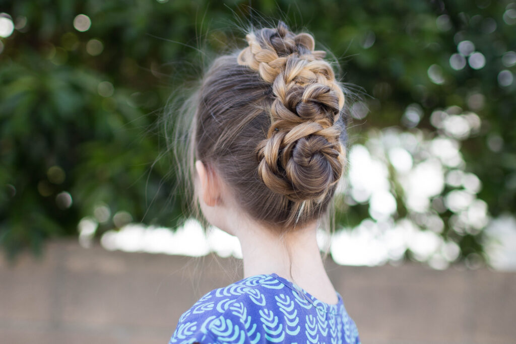 Side view of a little girl with long hair standing outside modeling "Triple Bun Updo" hairstyle