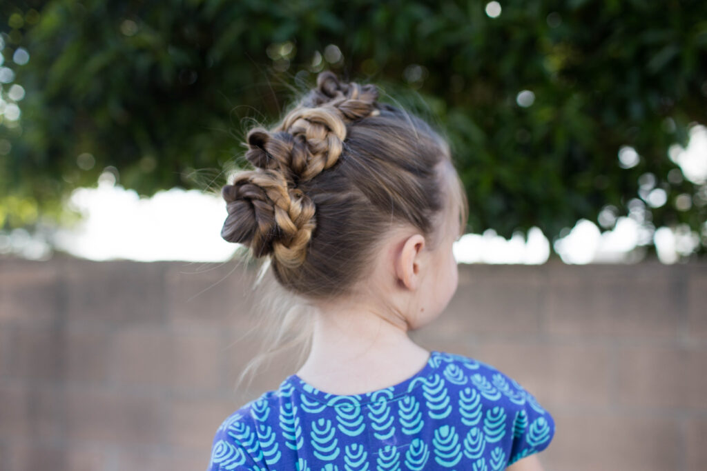 Side view of a little girl with long hair standing outside modeling "Triple Bun Updo" hairstyle