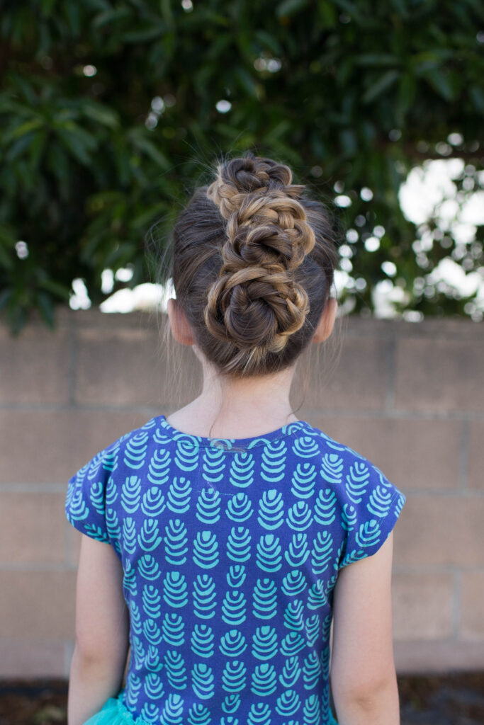 Back view of a little girl with long hair standing outside modeling "Triple Bun Updo" hairstyle