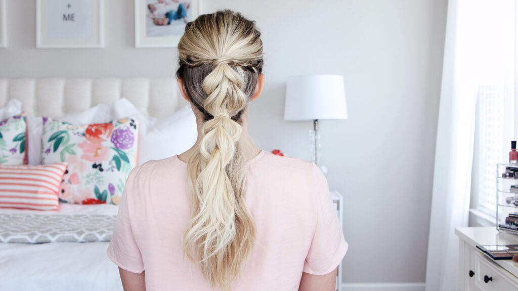 Back view of young woman standing in her room wearing pink shirt modeling "4-in-1 Pull Thru Braid" Hairstyle