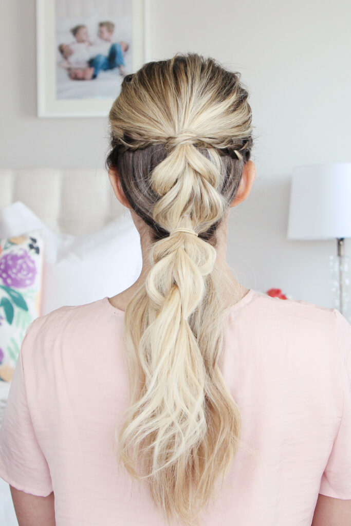 Back view of young woman standing in her room wearing pink shirt modeling "4-in-1 Pull Thru Braid" Hairstyle