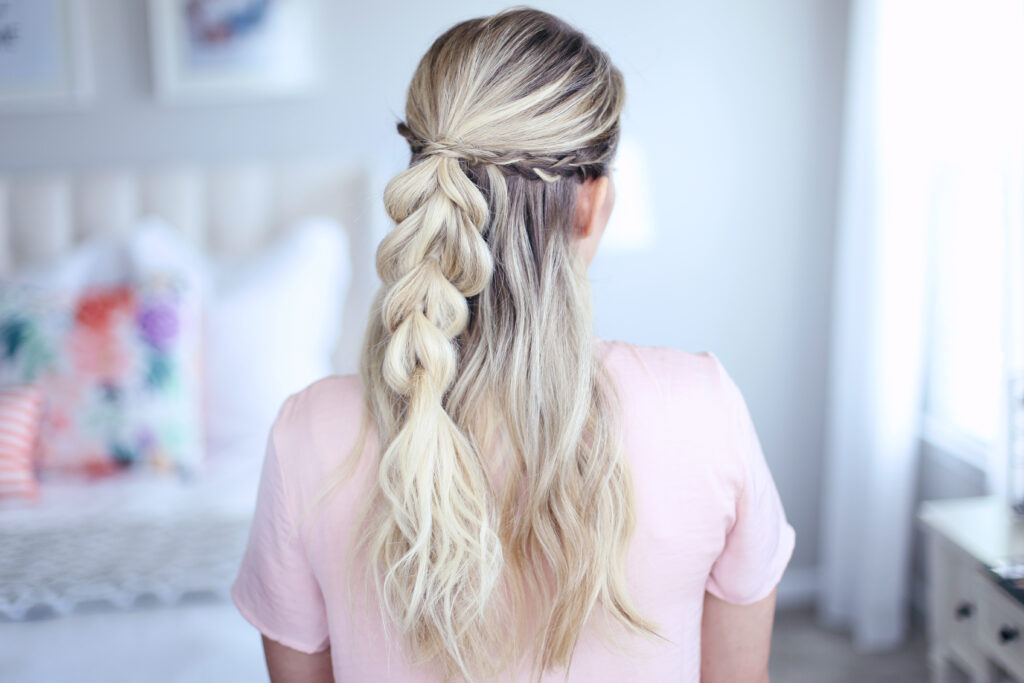 Back view of young woman standing in her room wearing pink shirt modeling "4-in-1 Pull Thru Braid" Hairstyle