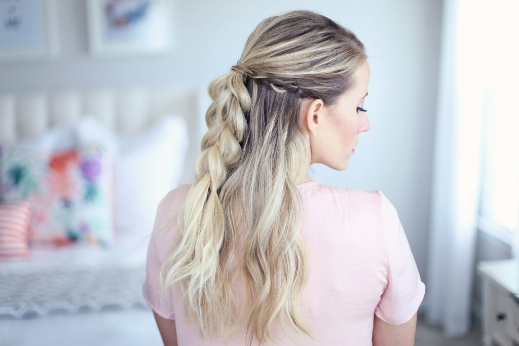 Side view of young woman standing in her room wearing pink shirt modeling "4-in-1 Pull Thru Braid" Hairstyle