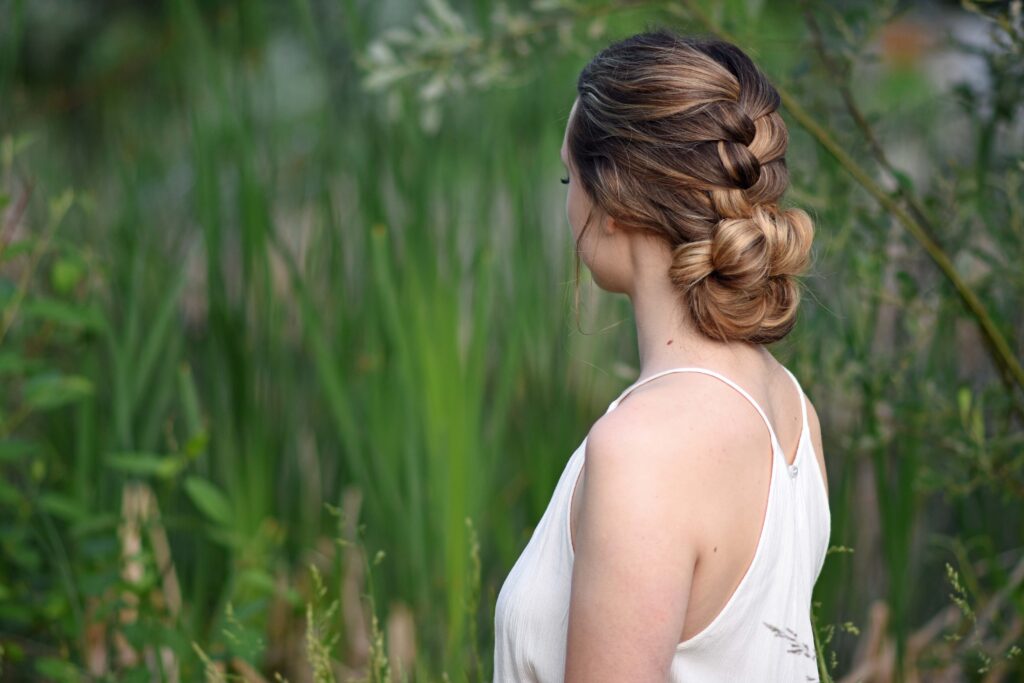 Side view of girl with a white dress standing outside in greenery and modeling "Knotted Braid Updo" hairstyle.