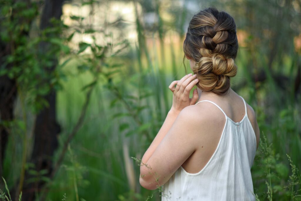 Side view of girl with a white dress standing outside in greenery and modeling "Knotted Braid Updo" hairstyle.