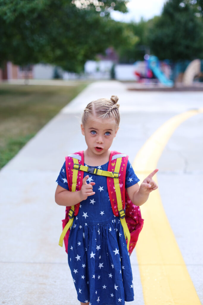 Little girl with a blue dress and white stars wearing a backpack on her way to school. 