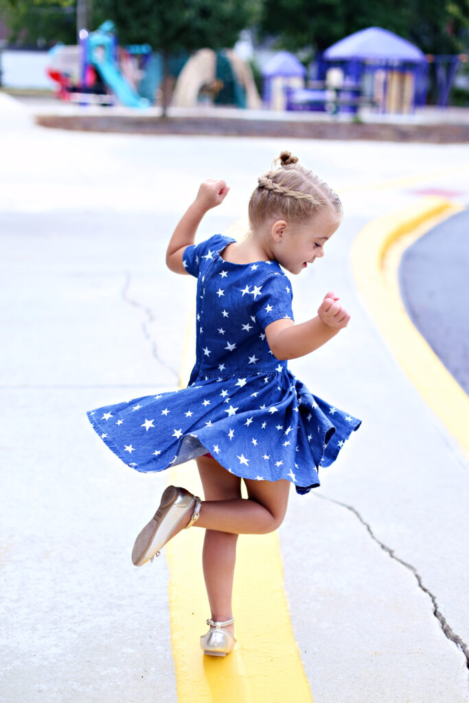 Little girl with blonde hair wearing a blue dress with white stars playing at the park. 