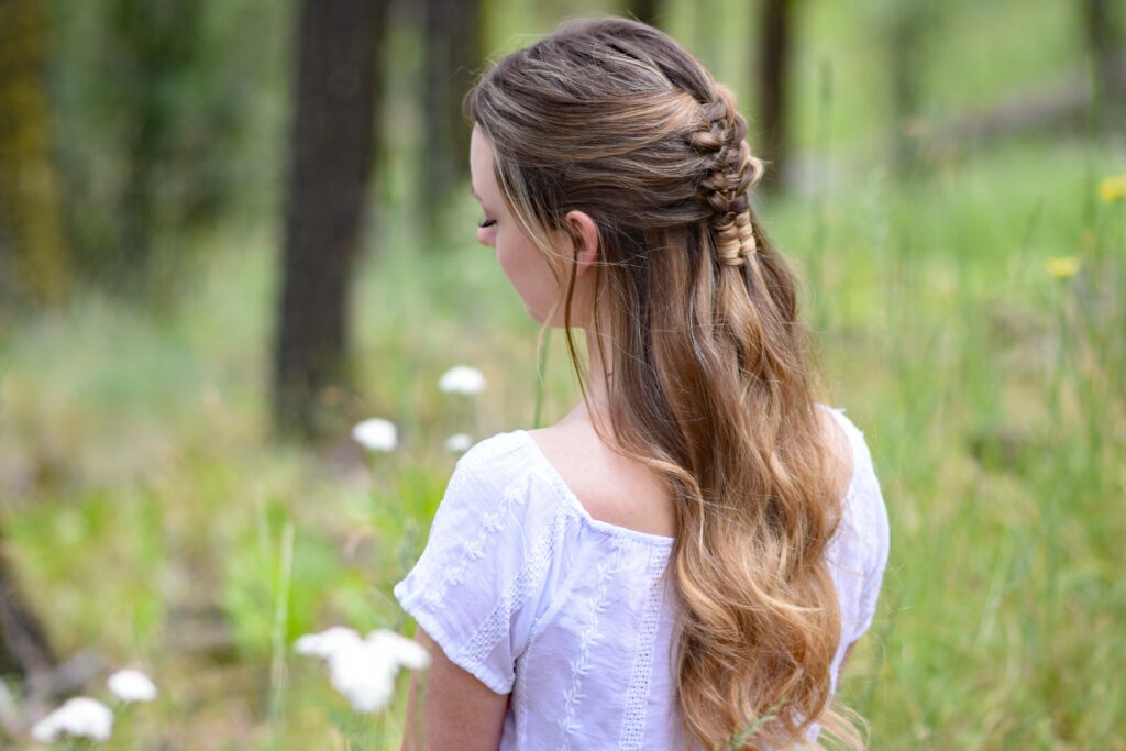 Side view of young girl standing in a meadow wearing a white shirt modeling "Floating Infinity Braid" hairstyle