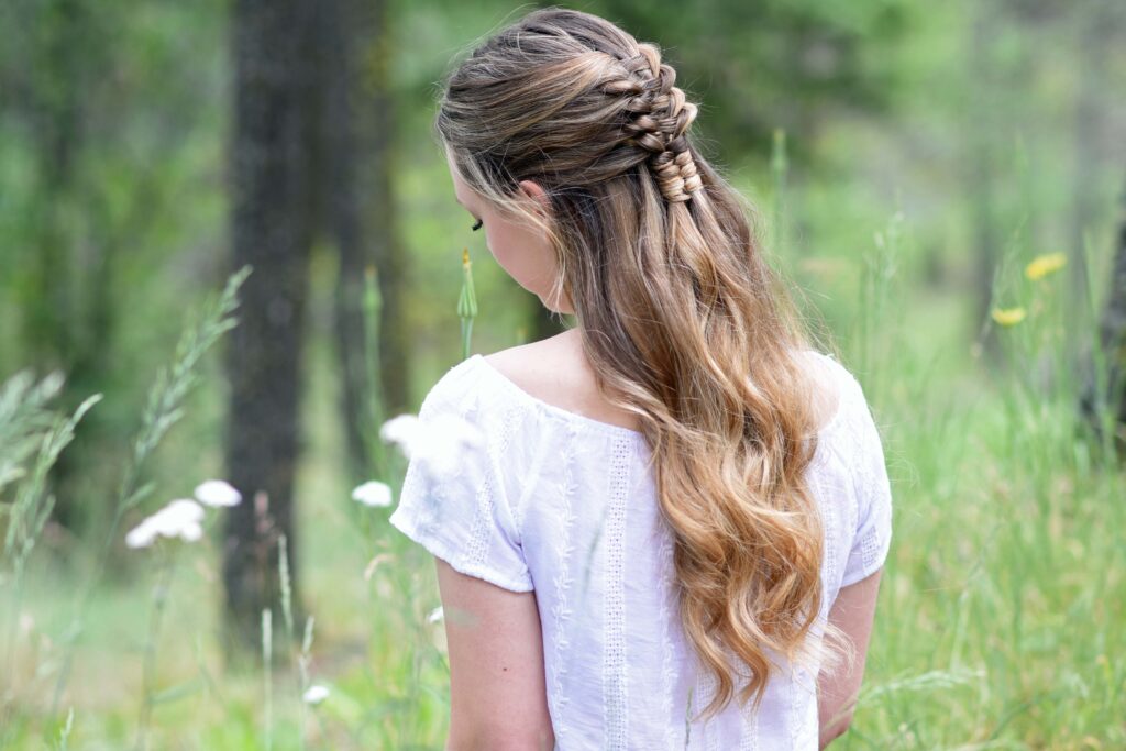 Side view of young girl standing in a meadow wearing a white shirt modeling "Floating Infinity Braid" hairstyle