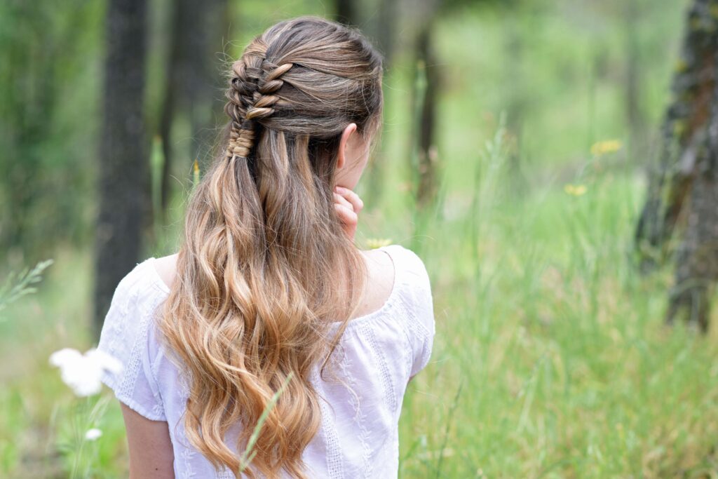 Side view of young girl standing in a meadow wearing a white shirt modeling "Floating Infinity Braid" hairstyle