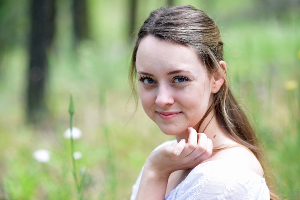 Portrait of a smiling young girl standing in a meadow wearing a white.