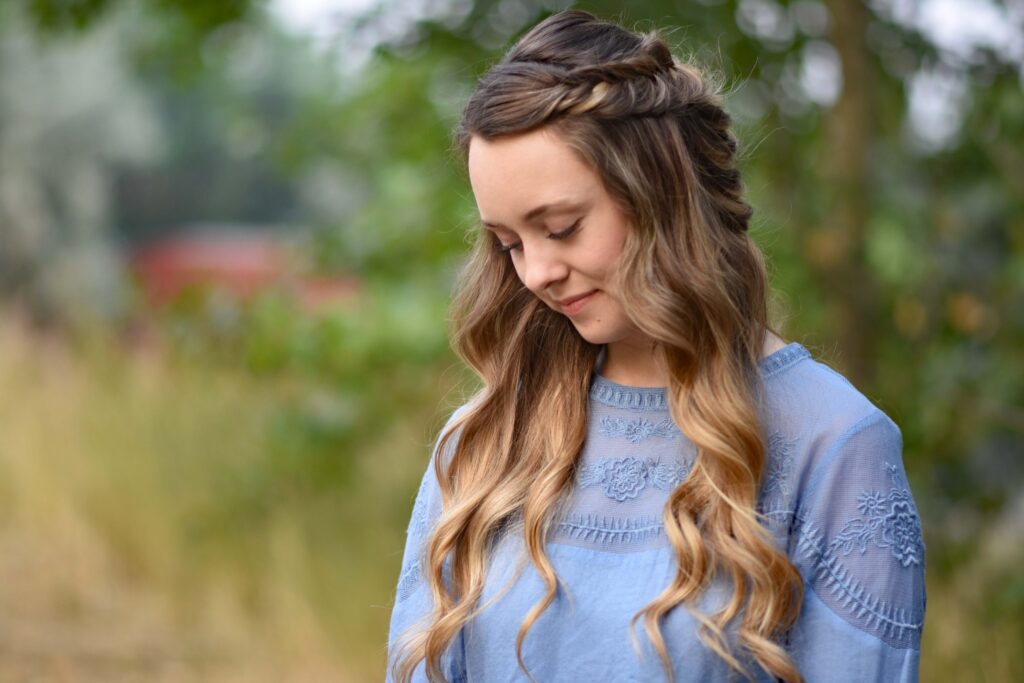 Portrait of young girl standing outside wearing a blue shirt modeling "Twisted Fishtail" hairstyle