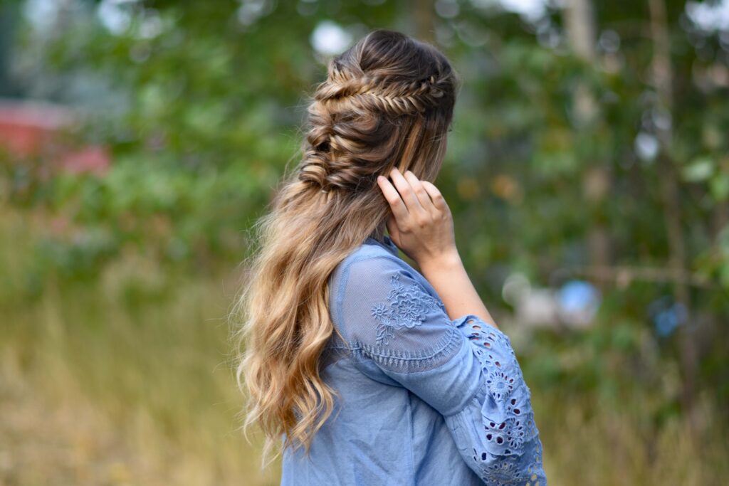 Sid view of young girl wearing a blue shirt standing outside modeling "Twisted Fishtail" hairstyle 