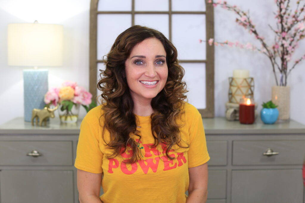 Portrait of woman with curly hair smiling sitting indoors wearing a yellow shirt