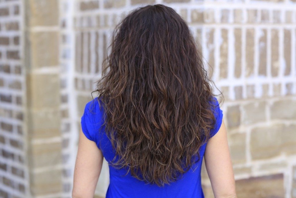 Back view of woman with the blue shirt standing in front of a brick background