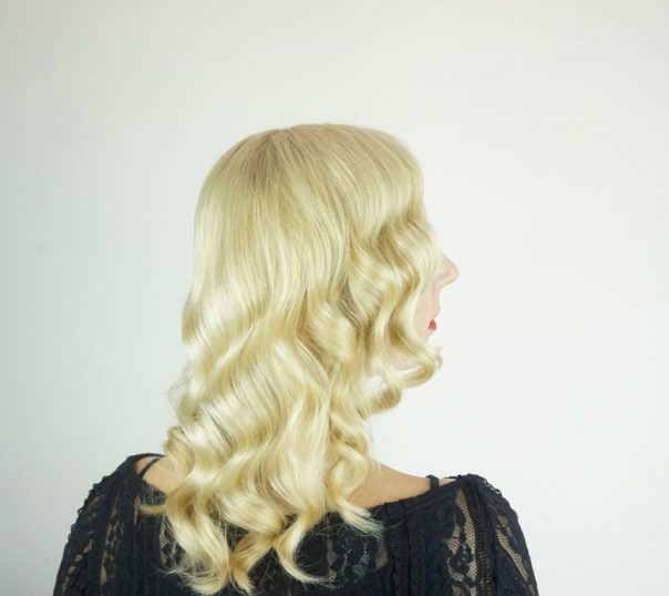 Back view of blonde woman wearing a black shirt in front of a white background wearing red lipstick