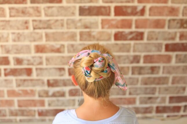 Back view of girl with a white shirt in front of brick background modeling "Braided Scarf Bun" hairstyle