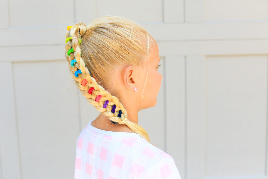 Side view of young girl standing outside with a pink shirt modeling multicolor "Banded Ponytail" hairstyle 