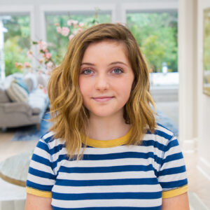 Portrait of girl smiling standing in her entryway wearing a blue striped shirt