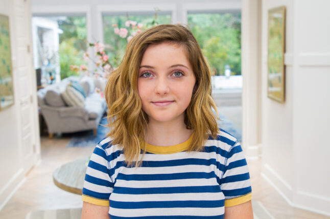 Portrait of girl smiling standing in her entryway wearing a blue striped shirt