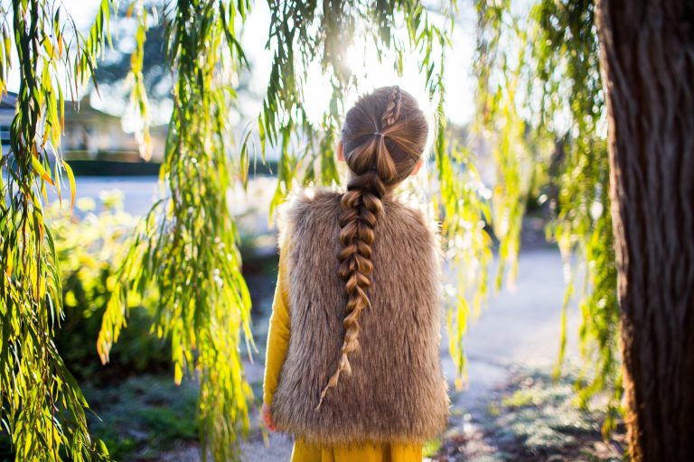 Back view of girl standing outside in forest modeling the "Dutch Pull-Thru Combo Braid" hairstyle