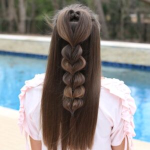 Back view of girl standing outside in front of the pool modeling the "Heart Pull-Thru Braid" hairstyle