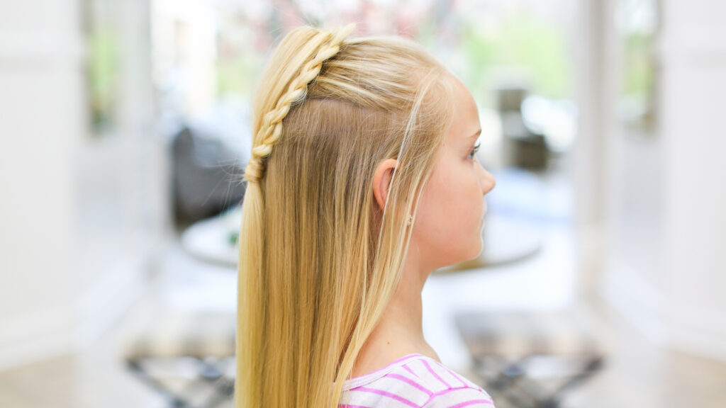 Profile view of girl with long blonde hair standing indoors modeling the "Fluffy Heart Braid" hairstyle