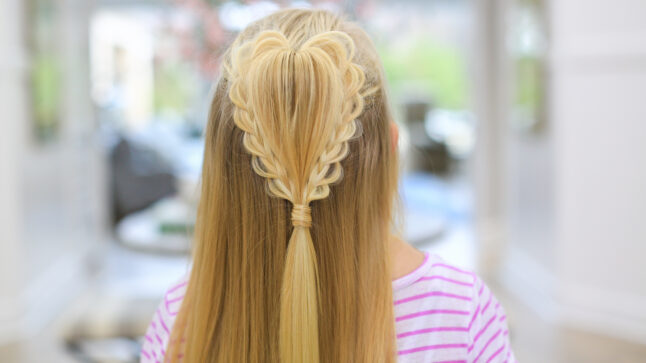 back view of a girl with long blonde hair standing indoors modeling the "Fluffy Heart Braid" hairstyle