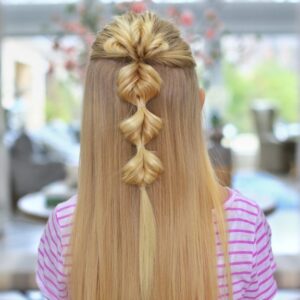 Back view of a young blonde girl standing indoors modeling the "Triple Flip Flips" hairstyle