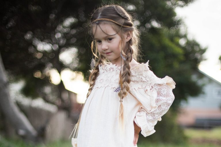 Girl with hands on her hips outside wearing a boho-inspired headband modeling "Boho Side Braids" hairstyle