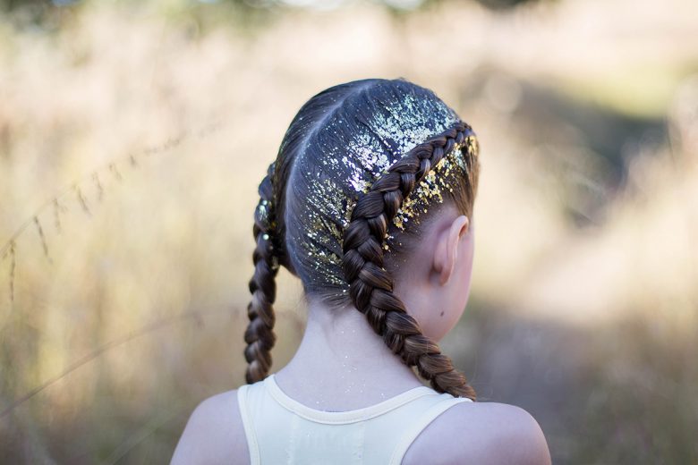 Back view of girl outside with gold glitter in her hair modeling "Dutch Glitter Braids" hairstyle