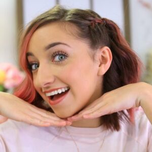 Girl with pink dyed hair indoors holding hands to her chin modeling "Side Pull Back" hairstyle.