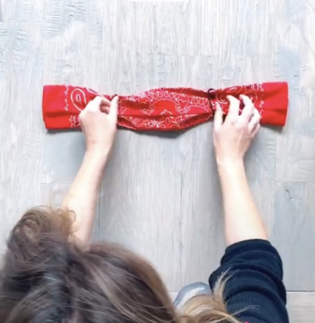 Woman is adjusting elastic hair ties on each side of the folded bandana on the floor