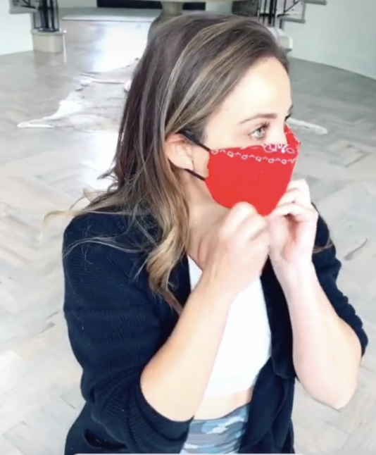 Side view of woman sitting on the floor wearing homemade bandana mask and her hands on the face mask.